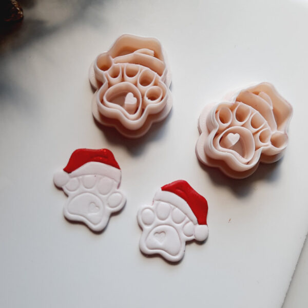 Holiday-themed clay cutter in the shape of a dog's paw with a Santa hat, used for creating Christmas polymer clay earrings.