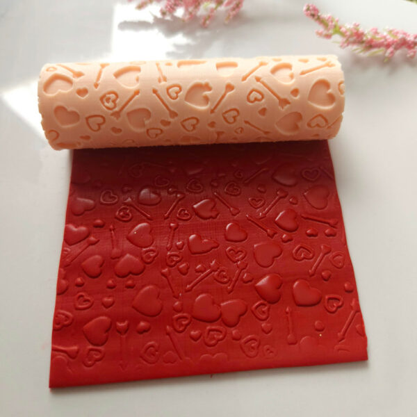 Texture roller with heart and arrow designs for Valentines' Day themed polymer clay earrings.